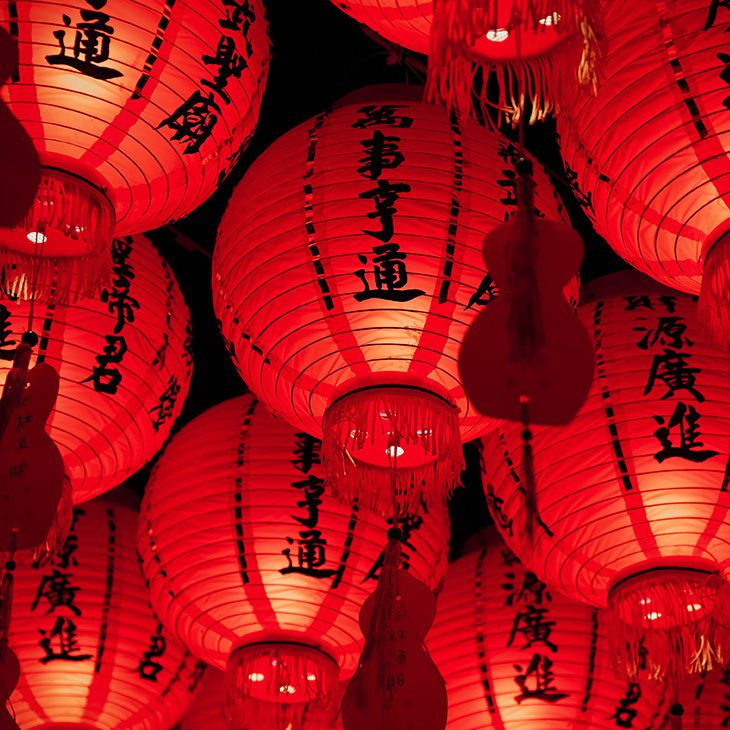 Red lanterns strung up on ceiling with chinese characters on the sides