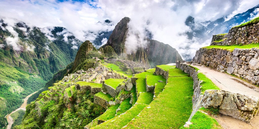 Machu Picchu in the distance against terraced, lush grass