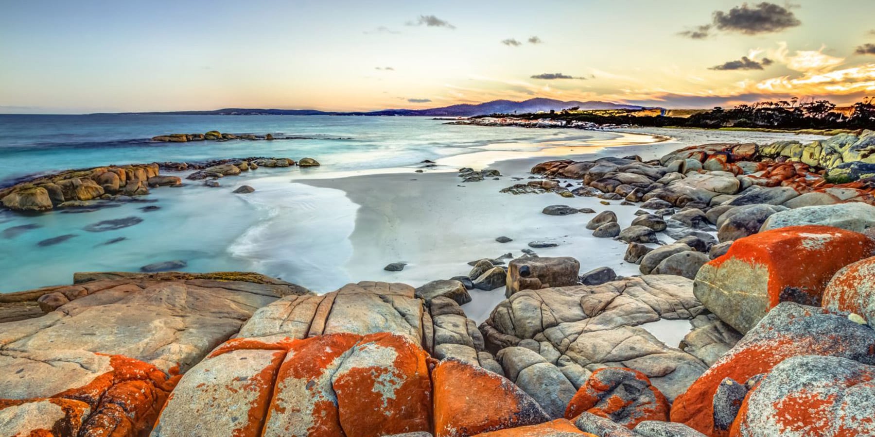 Craggy rocks tinged with vibrant orange with a view of waves along the beach - Bay of Fires Tasmania