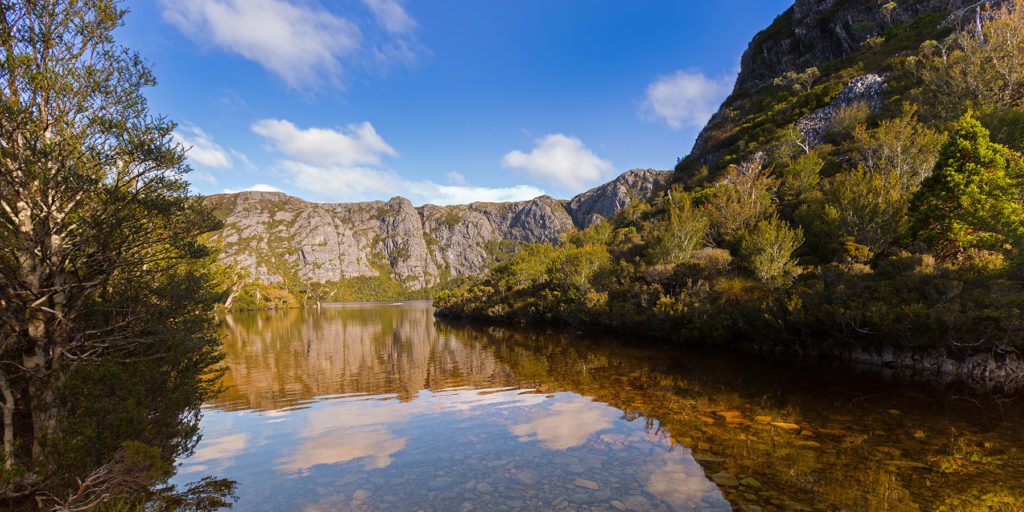 Still waters reflecting a blue sky surrounded by greenery. Crater Lake at Lake St Clair National Park. Tasmania