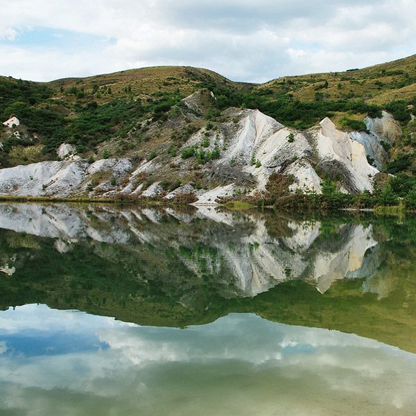 Water reflecting rocky and green hillside. New Zealand