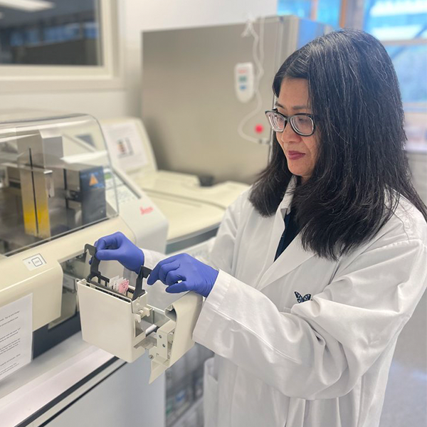 Woman in lab coat in a laboratory and opening up a machine. Head and Neck Cancer Foundation Aotearoa