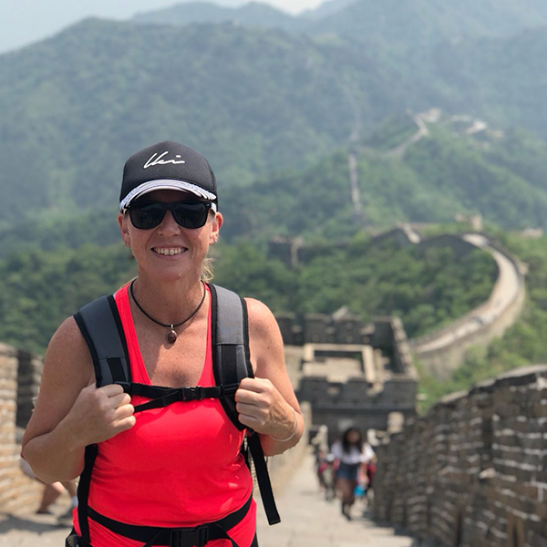 Smiling woman with trekking gear, with the Great Wall of China snaking out into the distance behind her.