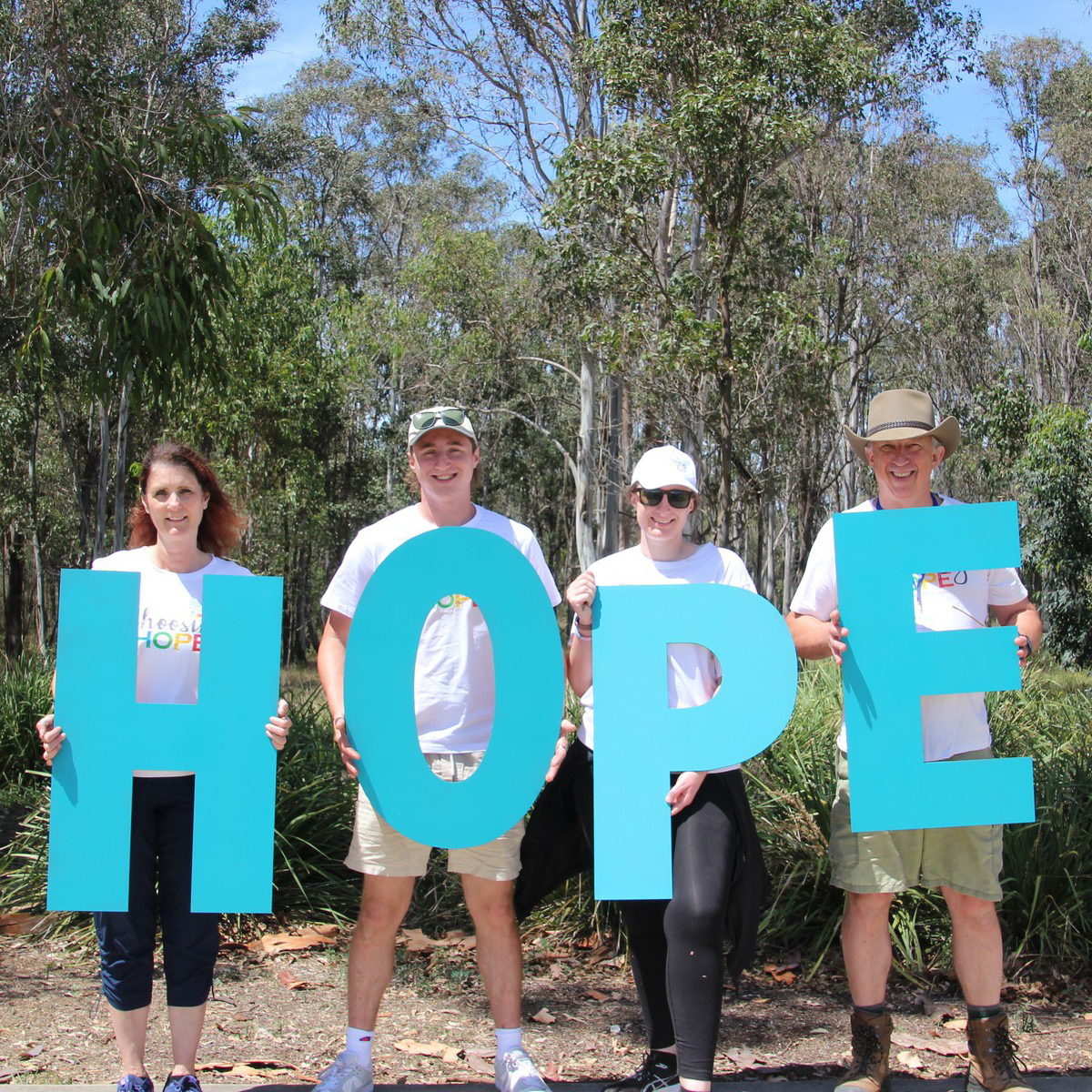 Bears of Hope - Bay of Fires Trek 2025: Four people holding a extra large letter each- spelling out HOPE in blue letters