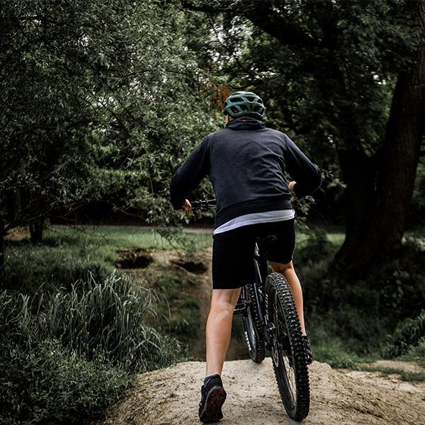 Back of a man on a bicycle outdoors, on a dirt path surrounded by greenery